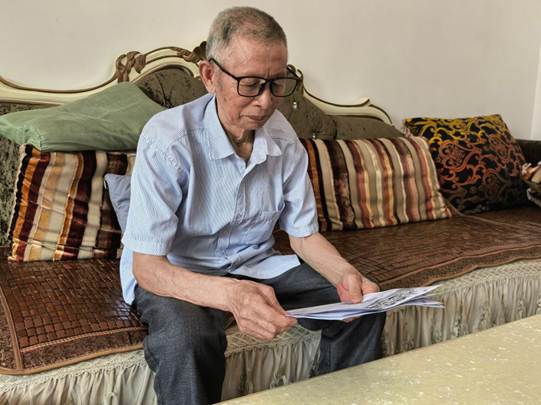 图为实践团成员入户走访，老人在家中认真阅读资助政策宣传手册